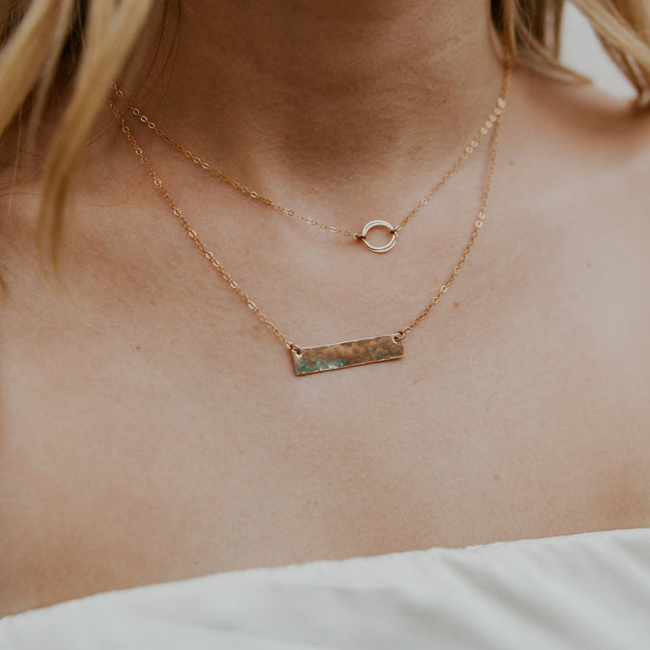 Close-up of a person wearing two gold necklaces on a neutral background