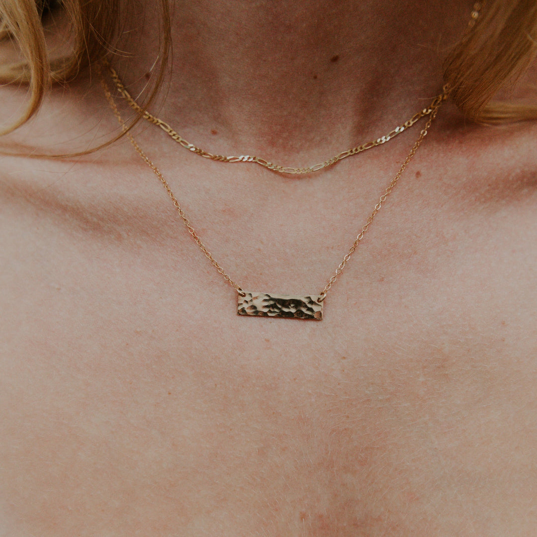 Gold necklace with a bar pendant on a person's neck