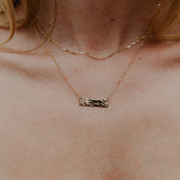 Gold necklace with a bar pendant on a person's neck