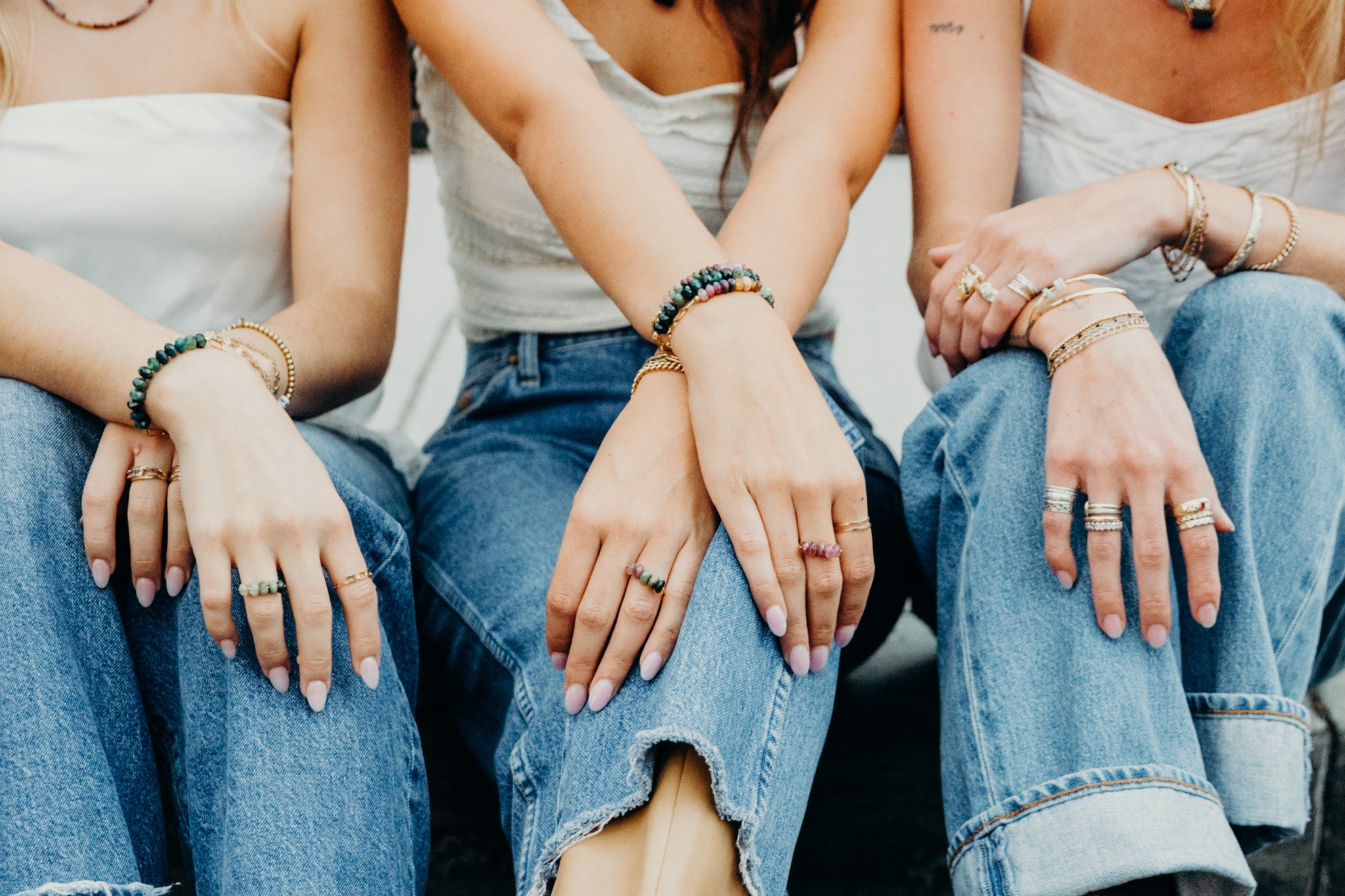 Three people sitting close together with hands on their laps, wearing jeans and bracelets.