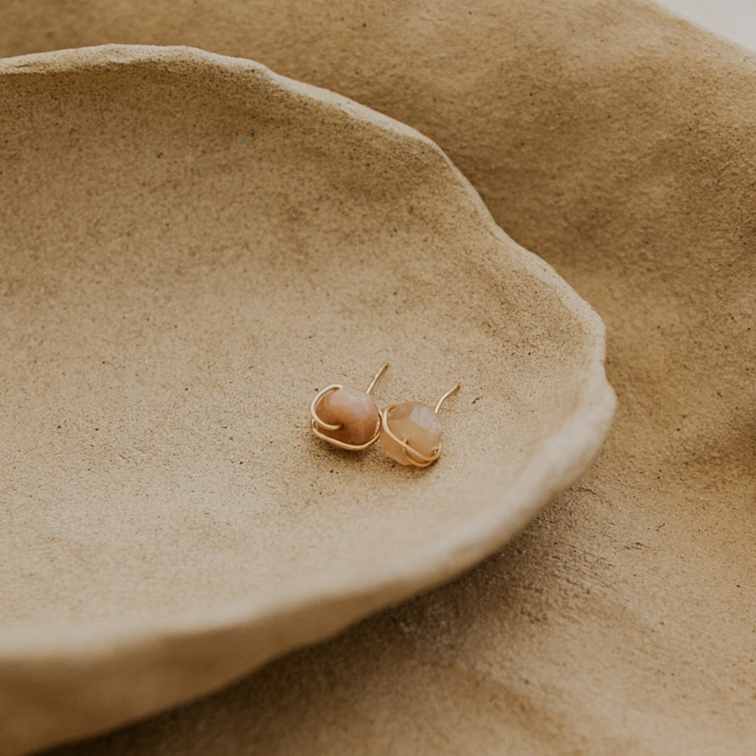 Pair of gold earrings on a textured beige surface