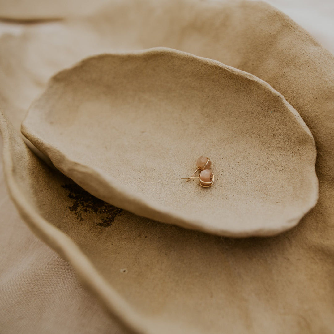 Small gold earring on a textured beige surface