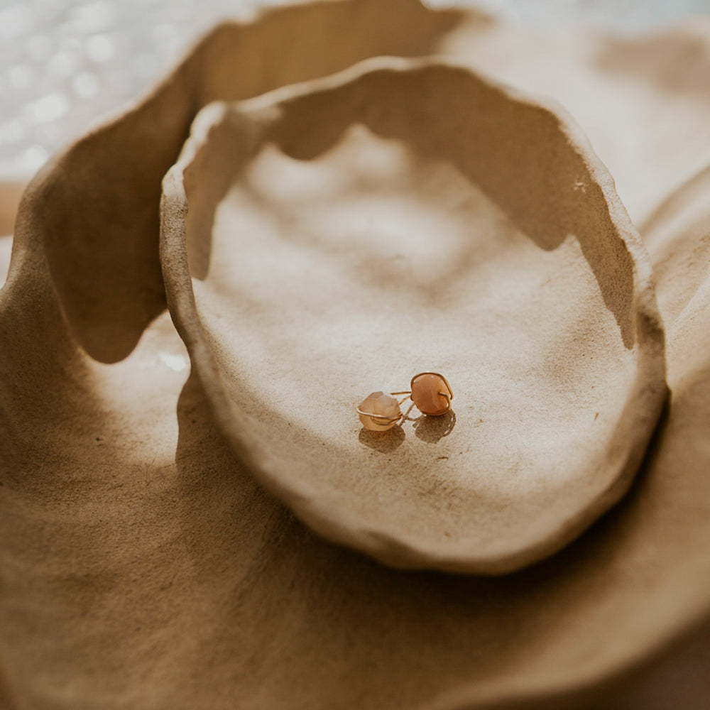 Small gold earring on a textured beige surface