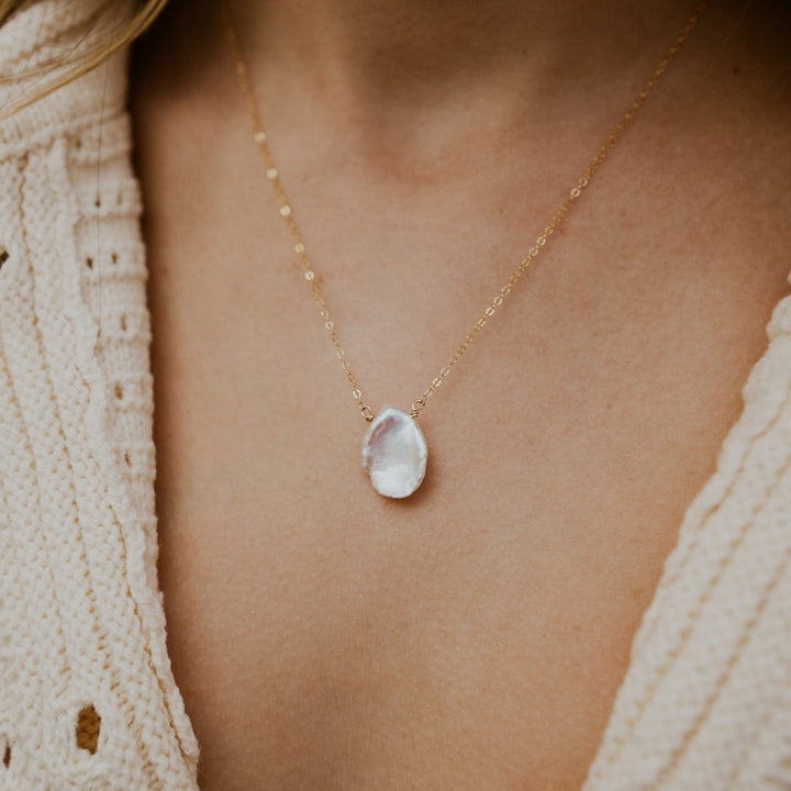 Necklace with a teardrop pendant worn by a person in a textured beige cardigan.