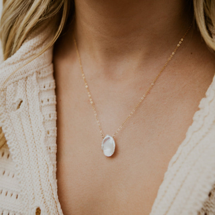 Necklace with a pendant worn by a person in a beige textured garment