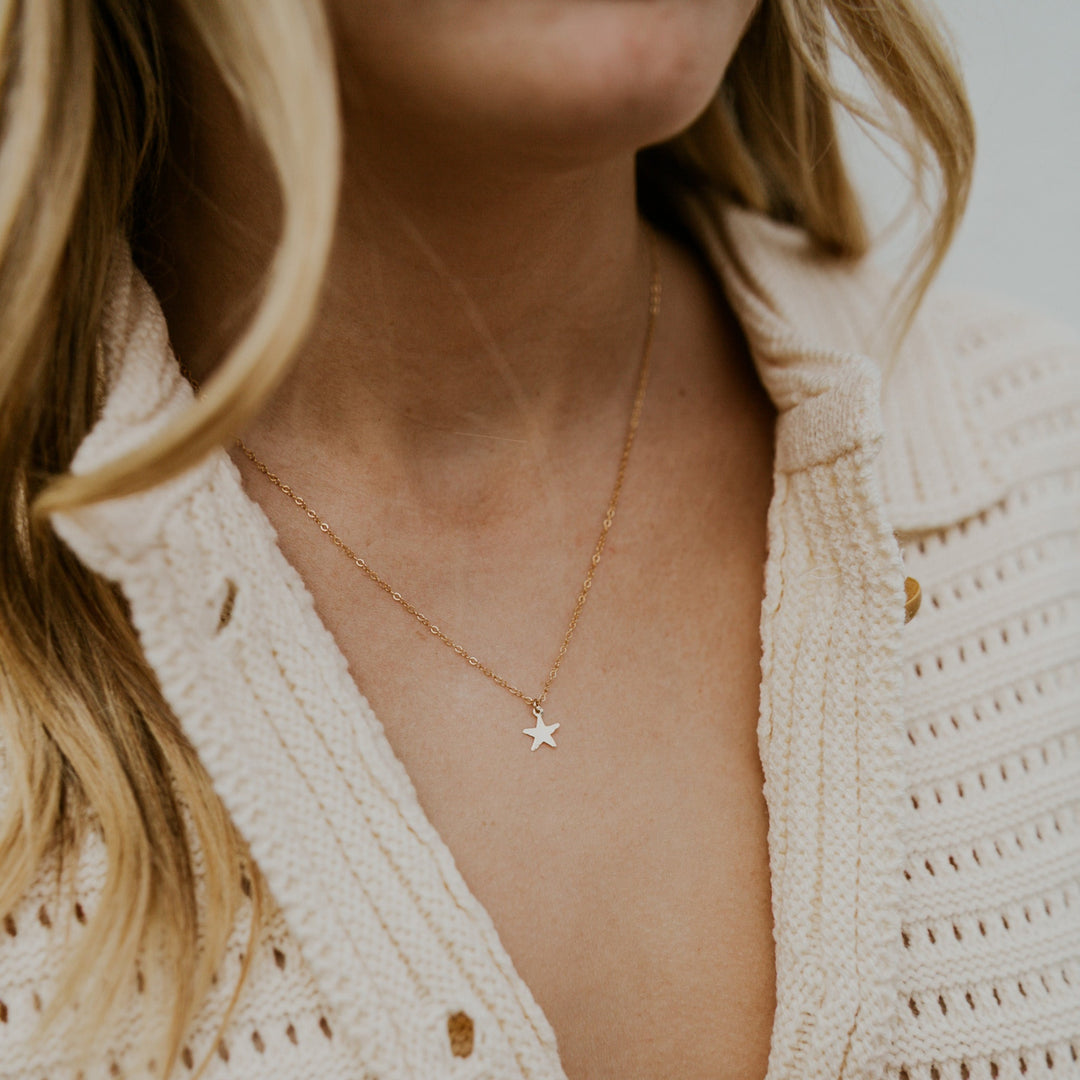 Close-up of a person wearing a delicate gold necklace with a star pendant, set against a neutral background.