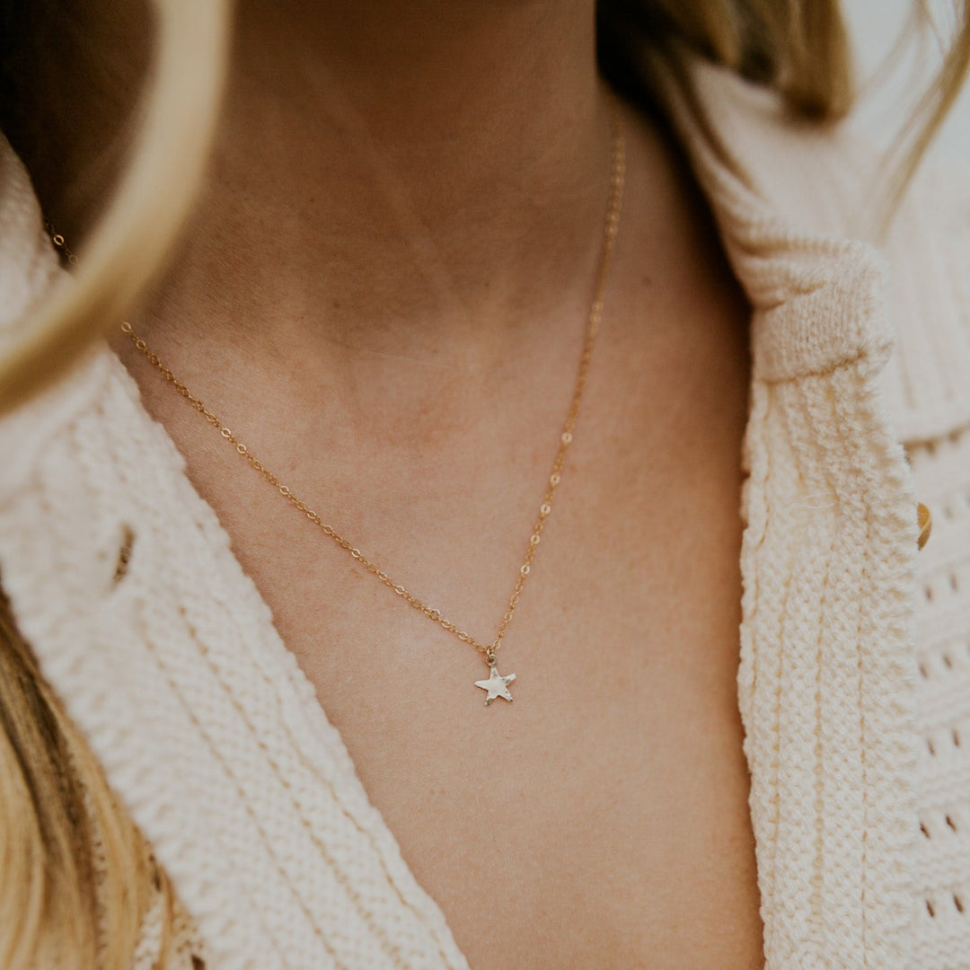 Close-up of a person wearing a delicate gold necklace with a star pendant, set against a neutral background.
