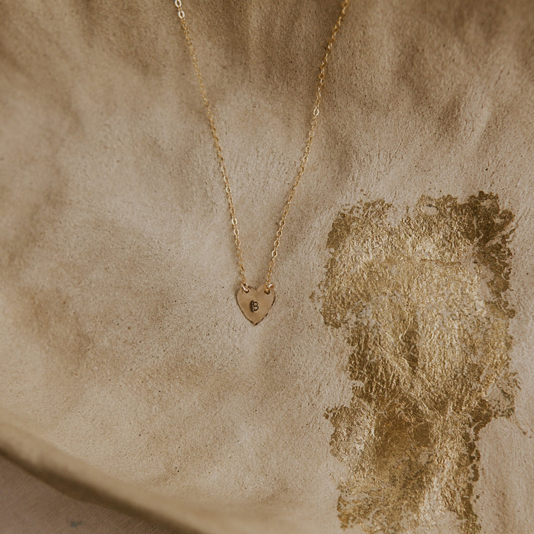 Gold necklace with a heart-shaped pendant on a textured beige background