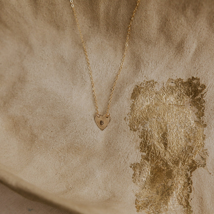 Gold necklace with a heart-shaped pendant on a textured beige background