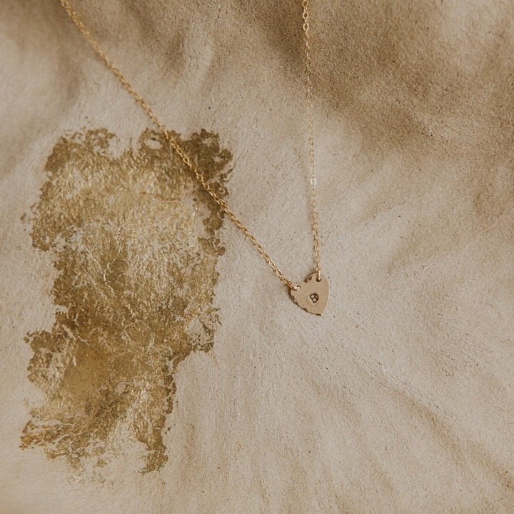 Gold necklace with a heart pendant on a textured beige surface
