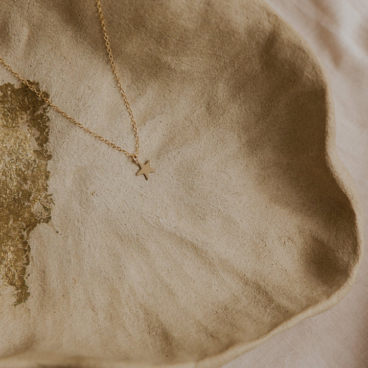 Gold necklace with a cross pendant on a textured beige surface