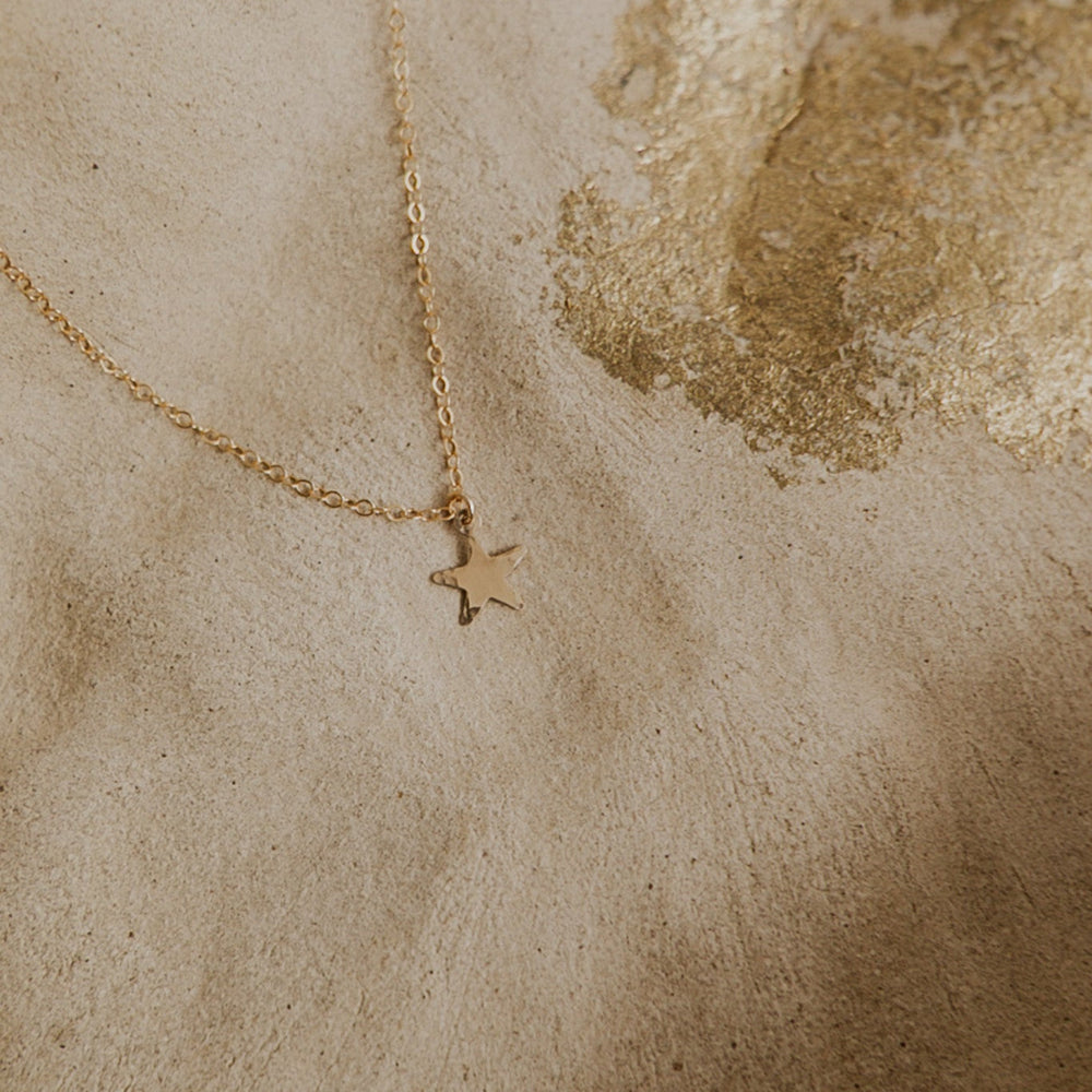 Gold star necklace on a textured beige surface