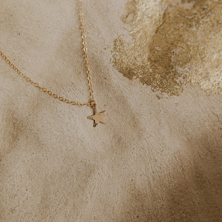 Gold star necklace on a textured beige surface