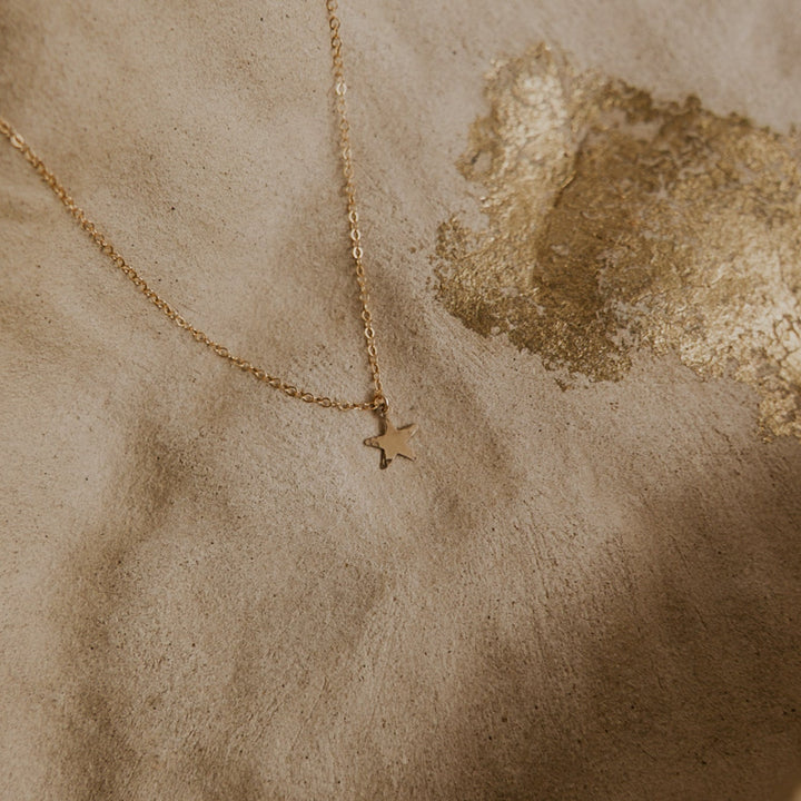Gold necklace with a star pendant on a textured beige surface