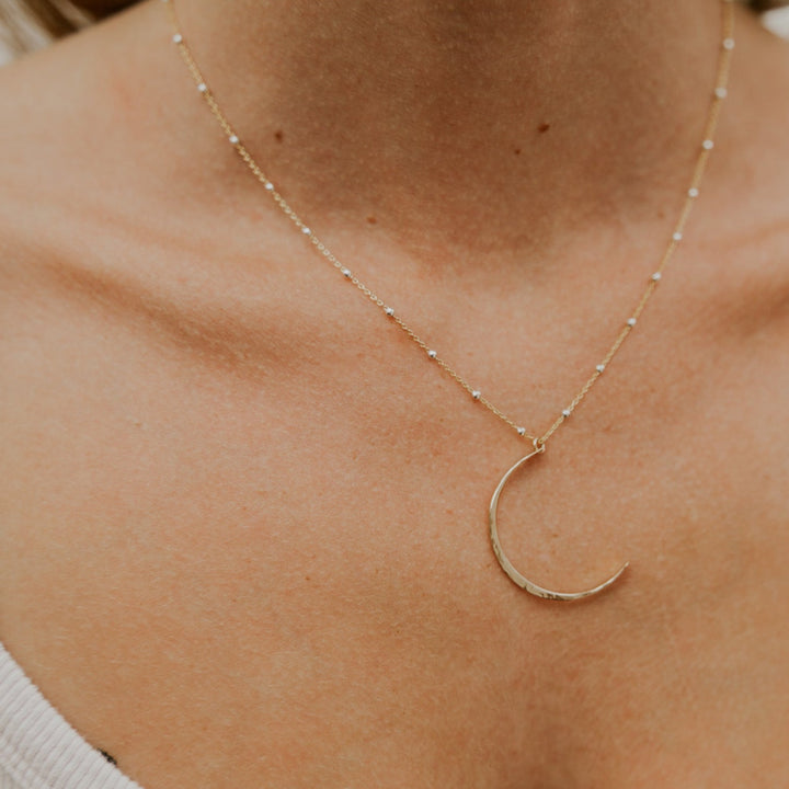 Gold crescent moon necklace on a person wearing a white tank top.