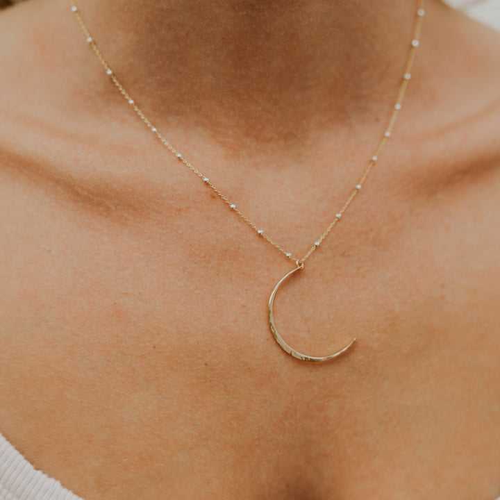 Gold crescent moon necklace on a person's neck