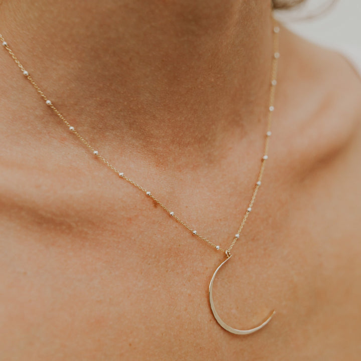 Gold necklace with a crescent moon pendant on a person's neck.