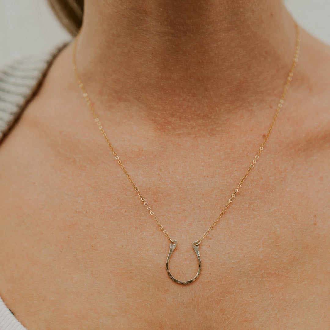 Gold necklace with a horseshoe pendant on a person wearing a white shirt.