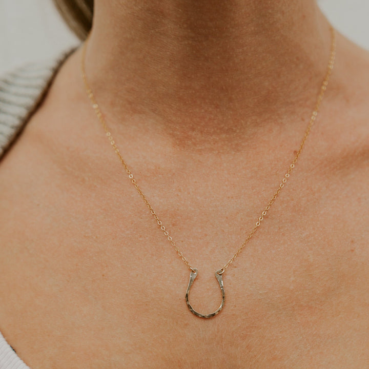 Gold necklace with a horseshoe pendant on a person wearing a white shirt.