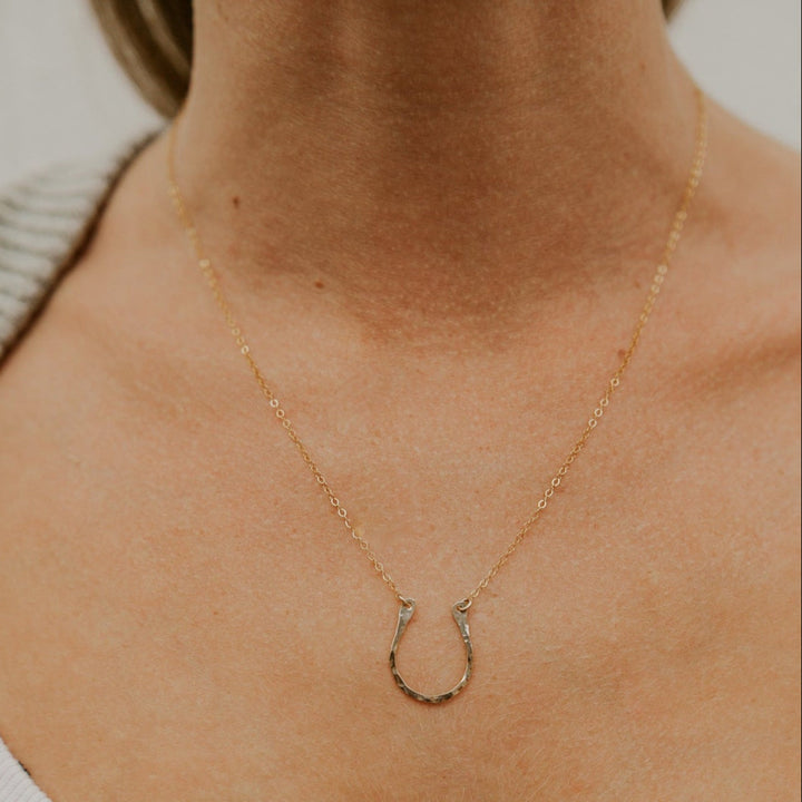 Gold necklace with a horseshoe pendant on a person's neck.