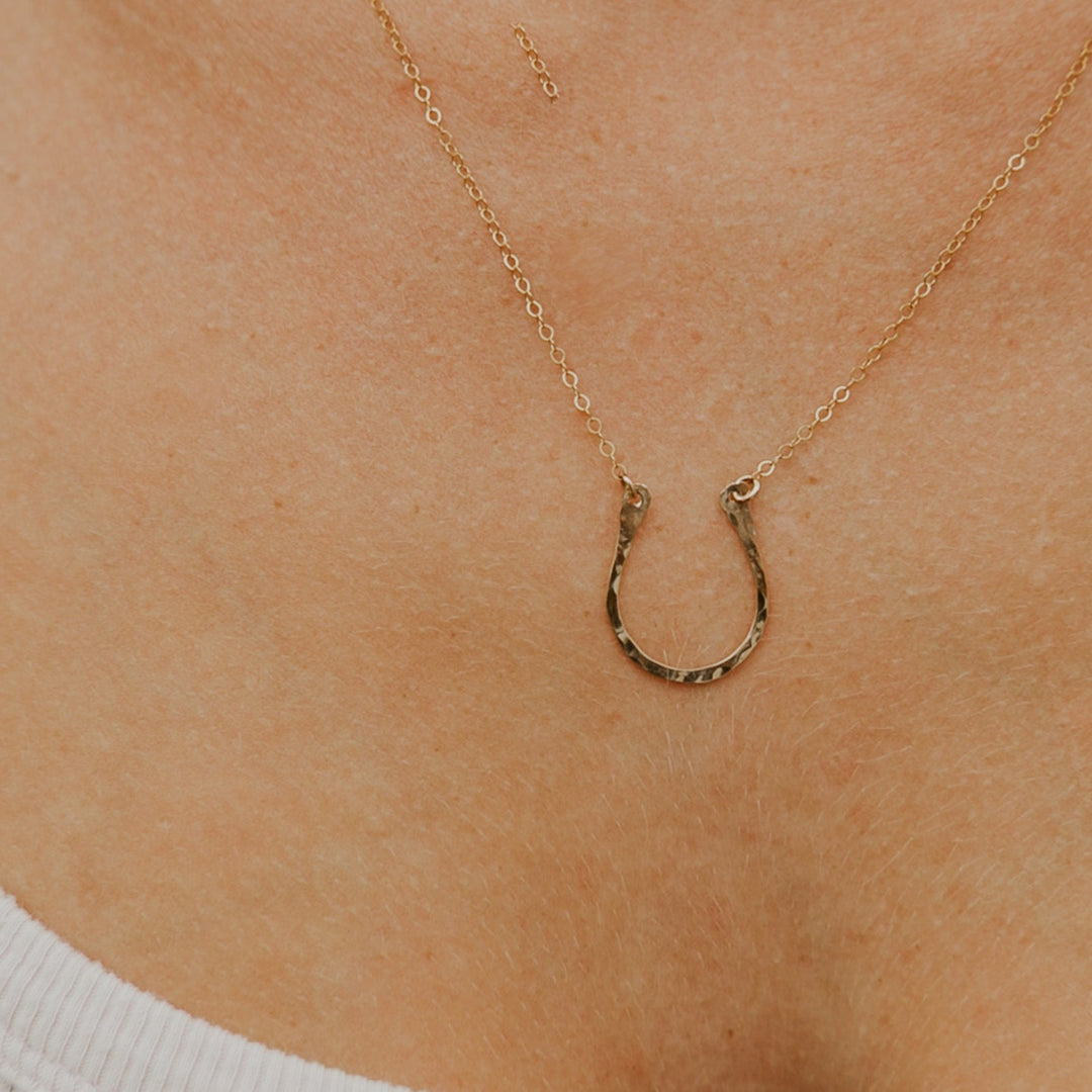 Gold horseshoe necklace on a person's neck