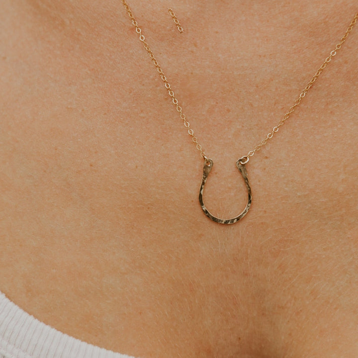 Gold horseshoe necklace on a person's neck