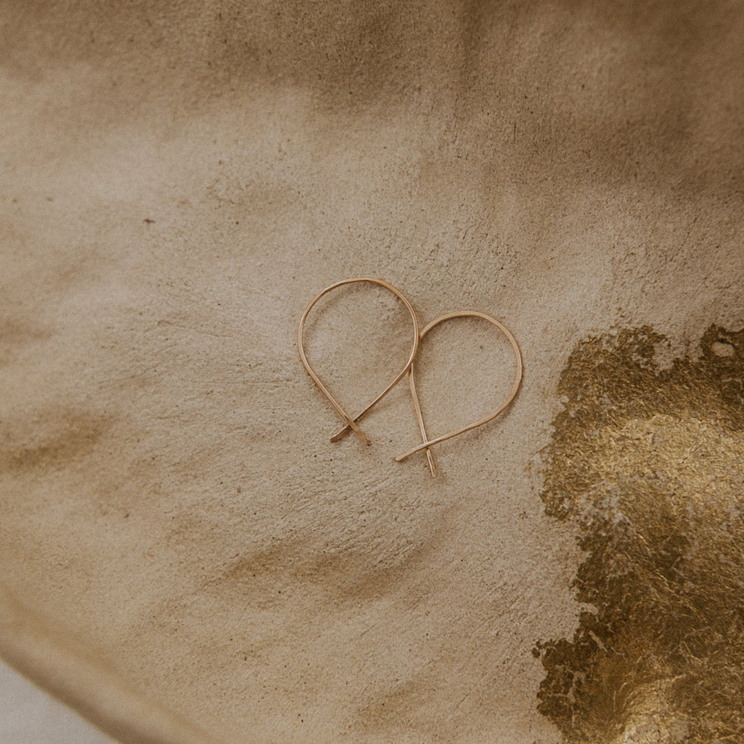 Gold heart-shaped earrings on a textured beige surface