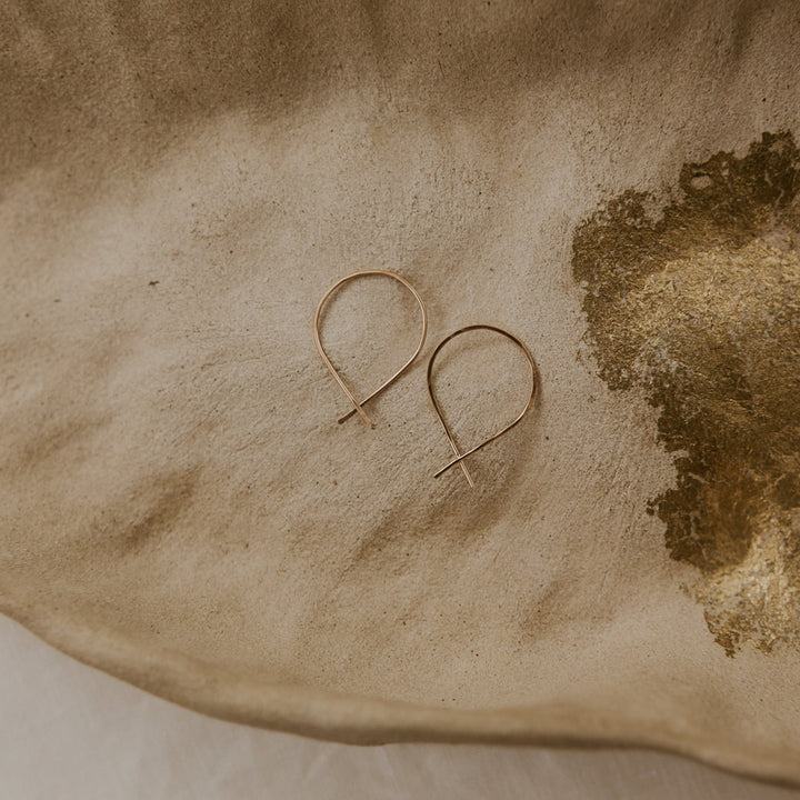 Pair of gold hoop earrings on a textured beige surface