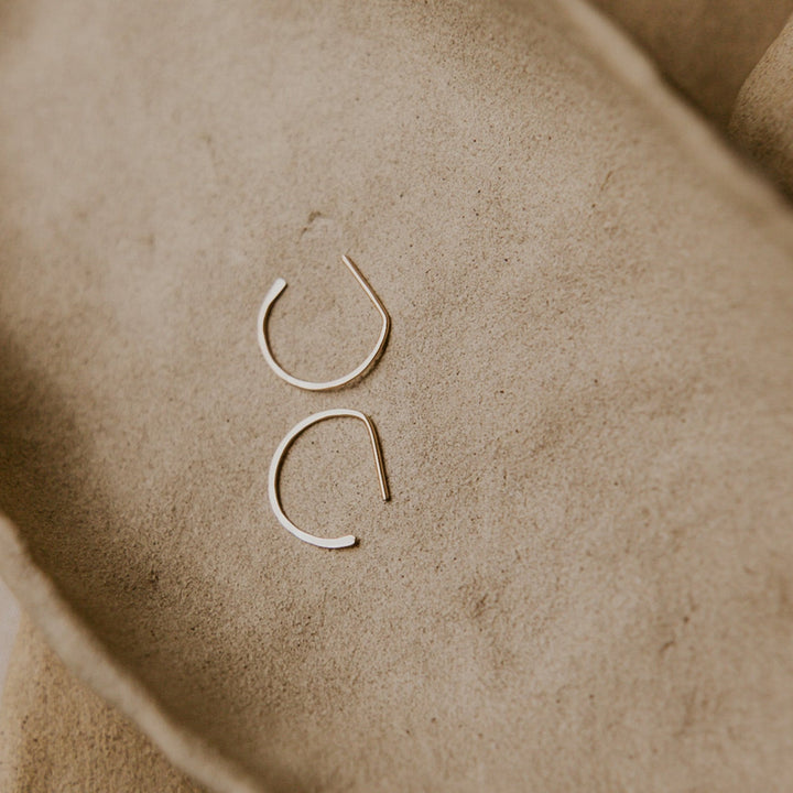 Two gold hoop earrings on a textured beige surface