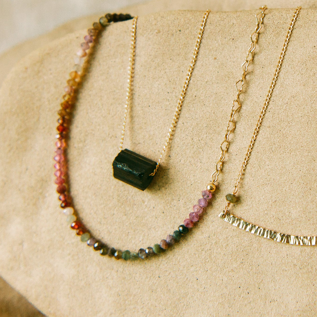 Aurora Necklace displayed on beige textured surface showing heart chain and centered spinel beads.