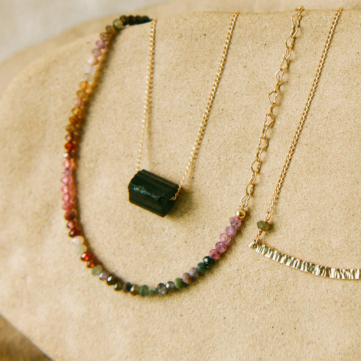 Aurora Necklace displayed on beige textured surface showing heart chain and centered spinel beads.