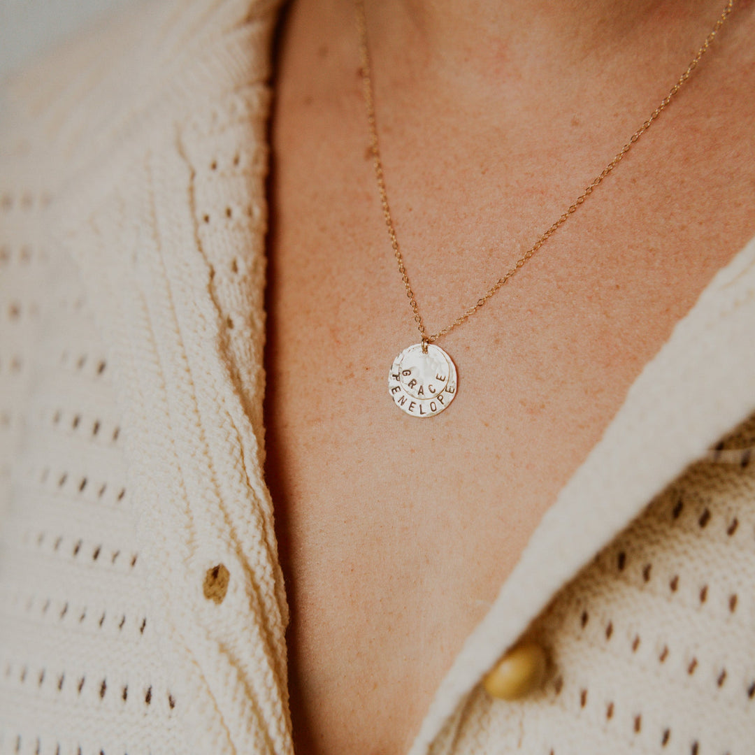 Gold necklace with a round pendant on a person wearing a beige cardigan.
