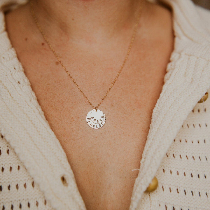 Necklace with a circular pendant worn by a person in a beige cardigan.