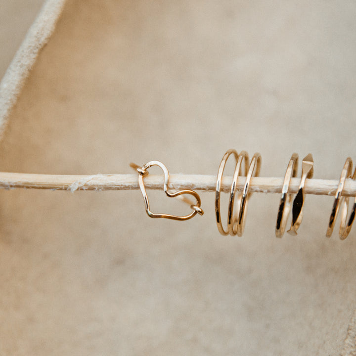 Gold heart-shaped and spiral rings on a wooden stick against a beige background