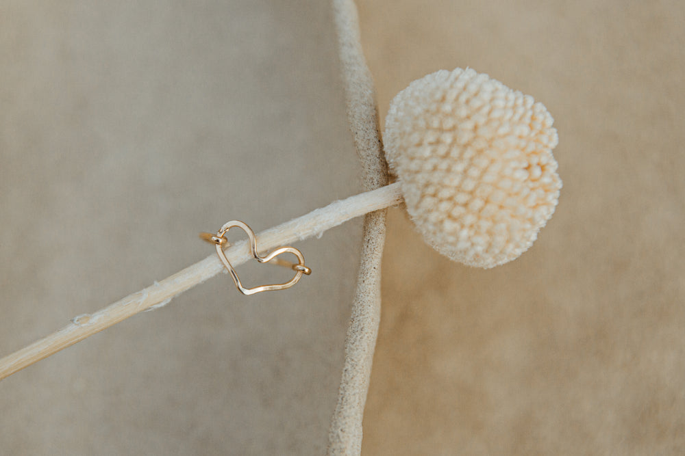 Gold heart-shaped earring on a branch with a beige background