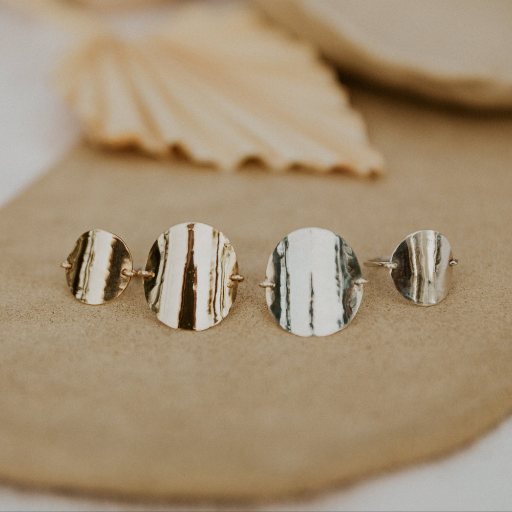 gold and silver rings in different sizes on a beige surface with natural elements in the background