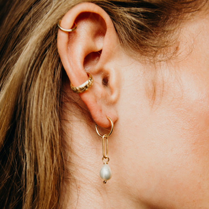 Close-up of an ear wearing gold hoop earrings with pearl drops.