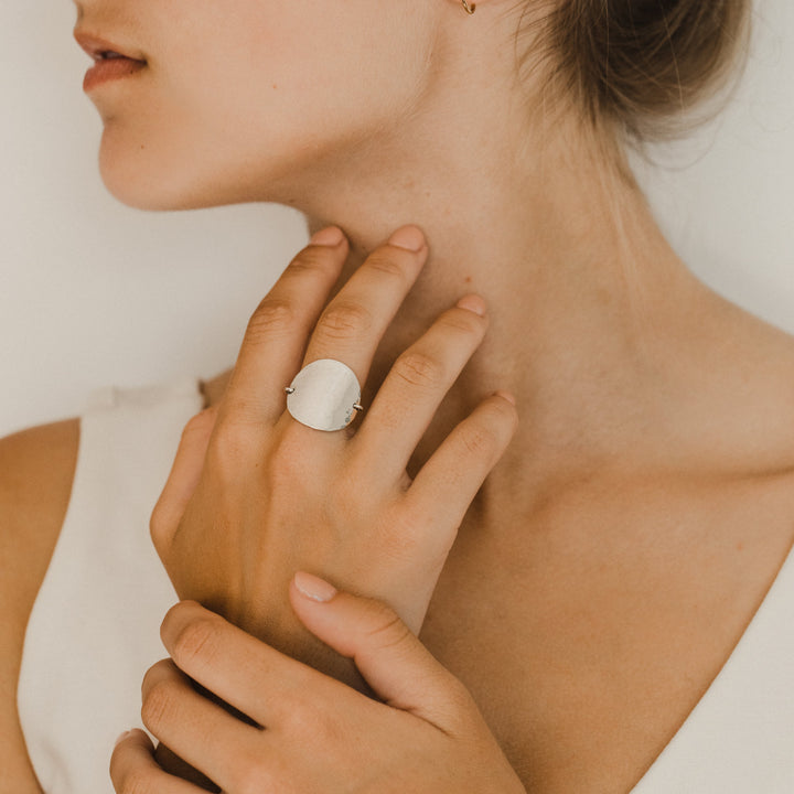Close-up of a woman wearing a silver disc ring on her hand with a neutral background
