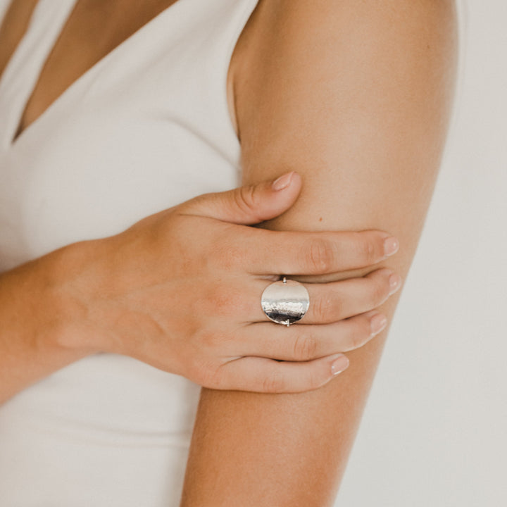 Close-up of a person wearing a silver disc ring on a blurred background