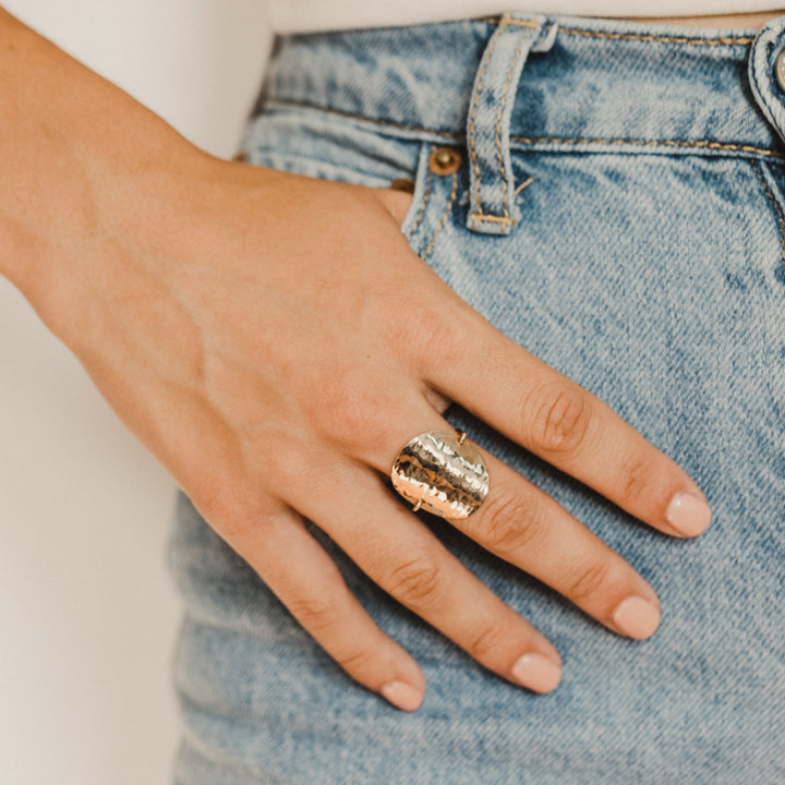 Hand wearing a gold disc ring on a light background