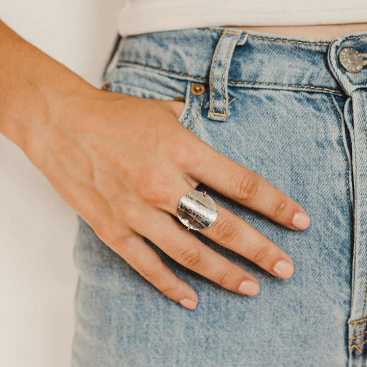 Hand wearing a silver disc ring on a light blue denim background