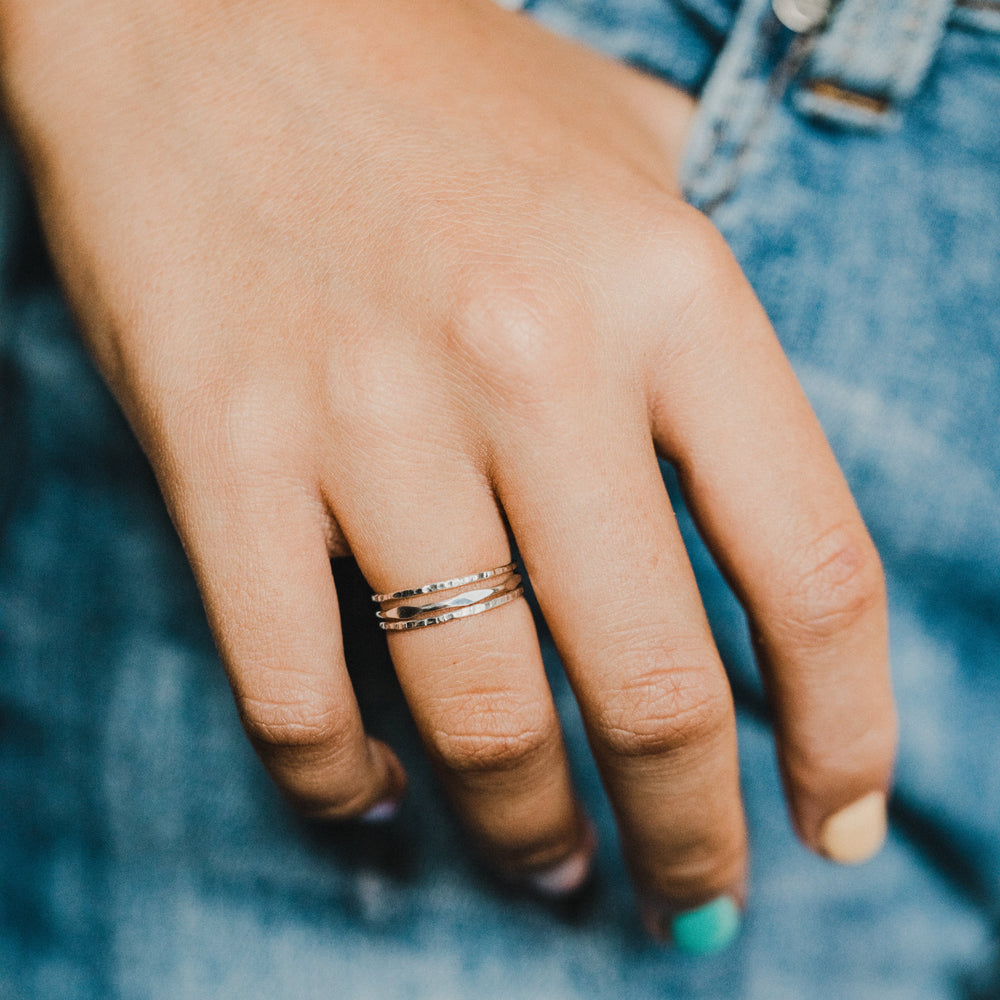 Close-up of a hand wearing 3 gold and silver  rings with a blurred denim background