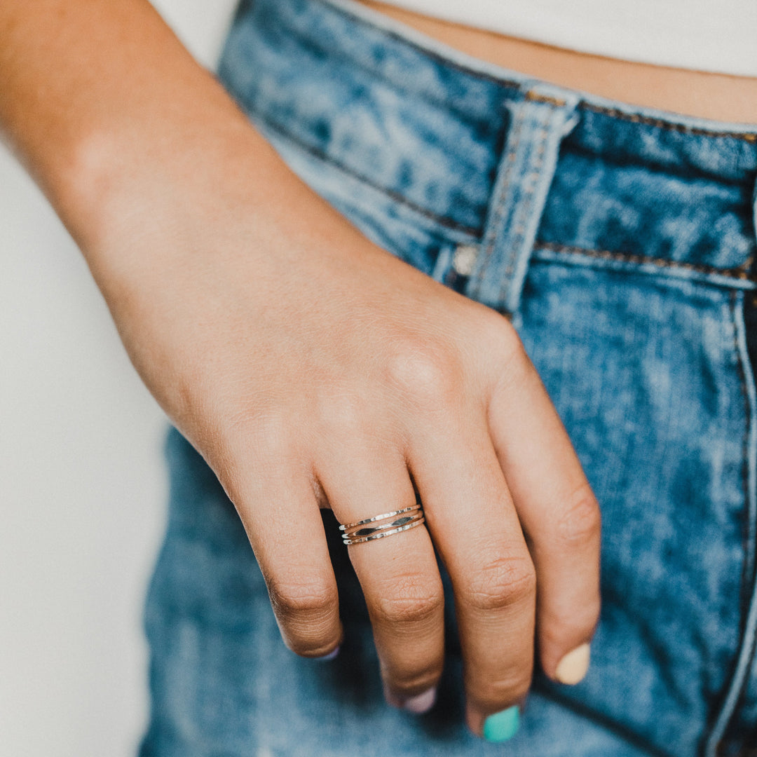 Hand wearing a 3 stacked rings with blue jeans and a white top