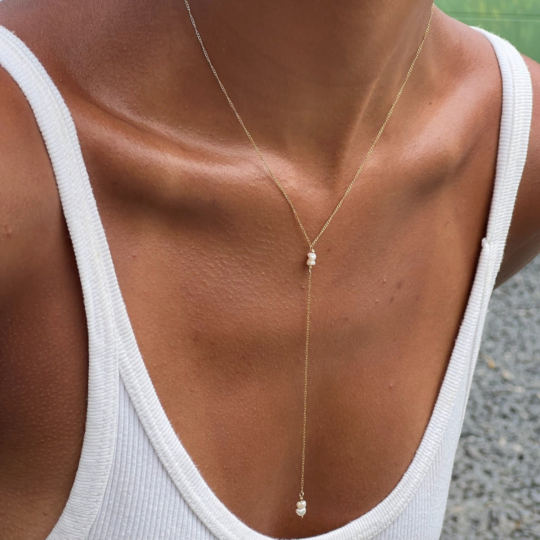 A person wearing a white tank top showcasing a gold-filled Y-necklace with freshwater pearl drops.
