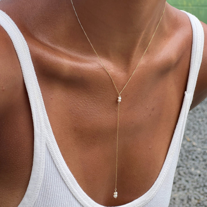 A person wearing a white tank top showcasing a gold-filled Y-necklace with freshwater pearl drops.