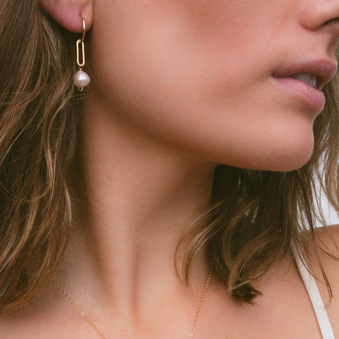 Close-up of a woman wearing a gold necklace with a pearl pendant and matching earrings.