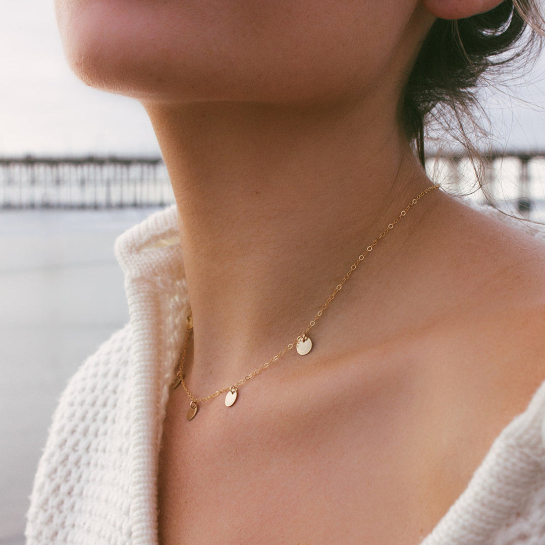 Close-up of a person wearing a delicate gold necklace with small round pendants.
