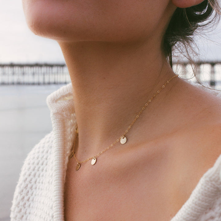 Close-up of a person wearing a delicate gold necklace with small round pendants.