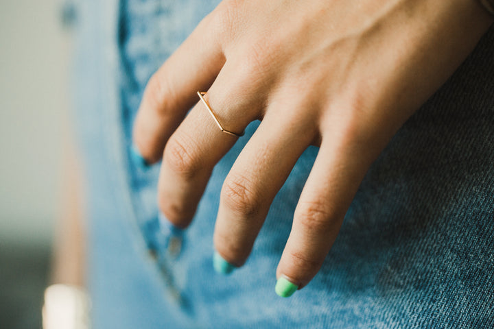 Close-up of a hand with a gold hand shaped ring on a denim background