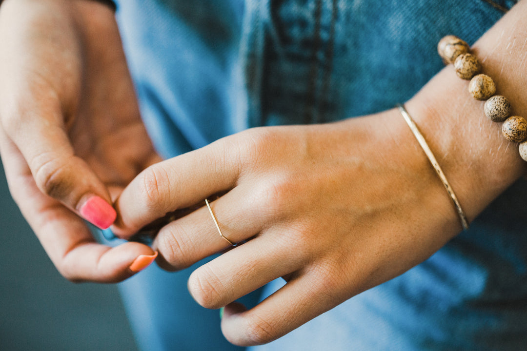 Close-up of hands with a gold hand shaped ring and bracelets on a blurred background